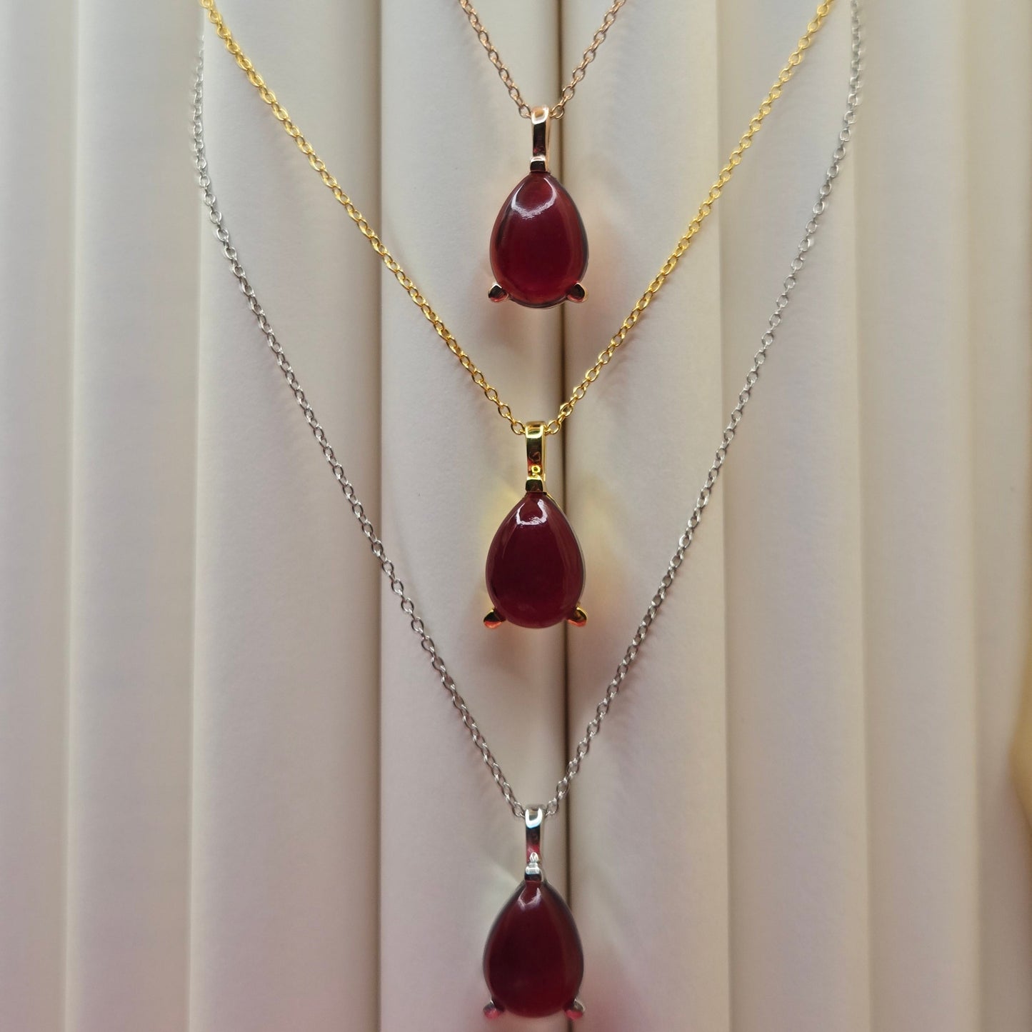 Gold-plated chain necklace featuring a smooth teardrop-shaped deep maroon gemstone pendant, styled against a soft neutral backdrop for an elegant and minimal look.