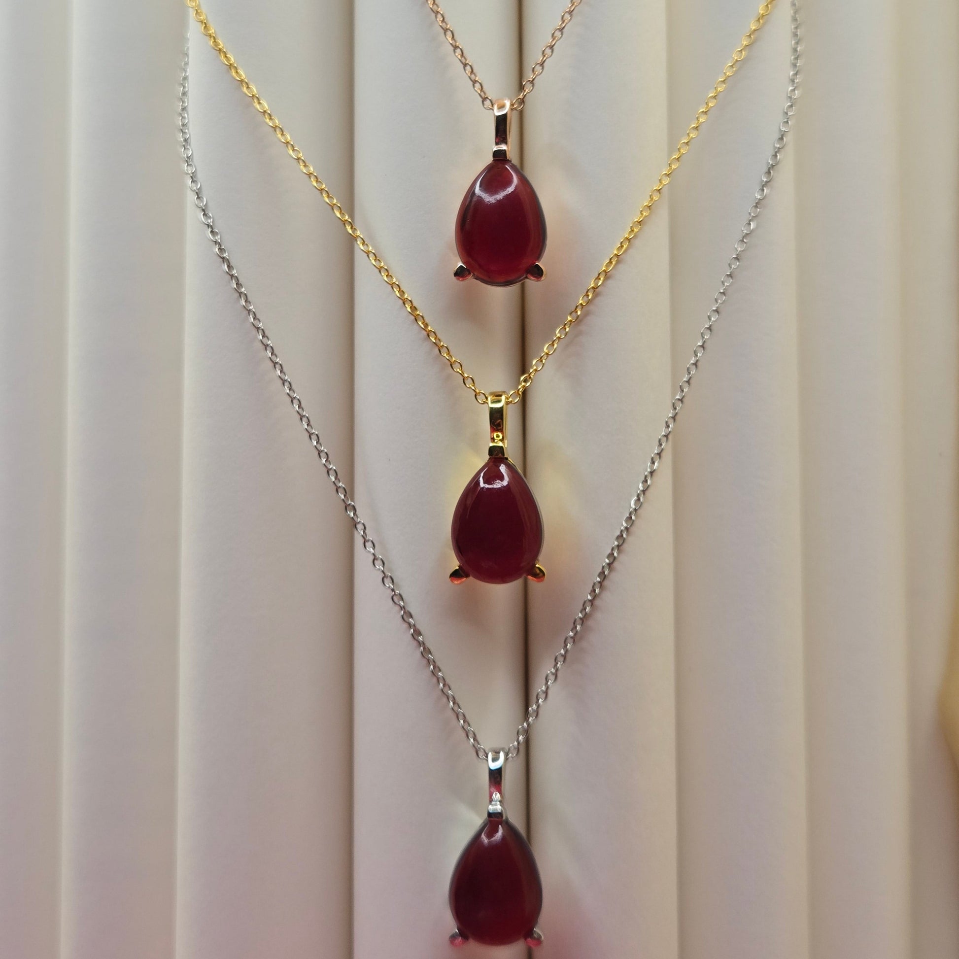 Gold-plated chain necklace featuring a smooth teardrop-shaped deep maroon gemstone pendant, styled against a soft neutral backdrop for an elegant and minimal look.