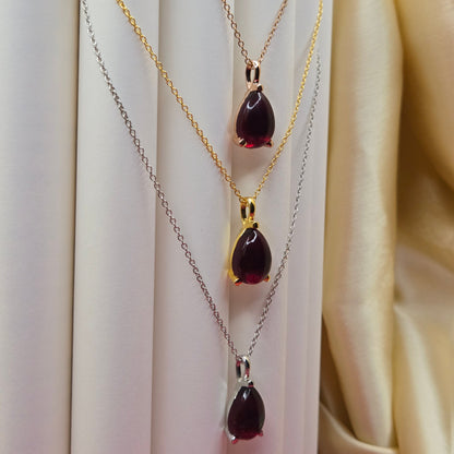 Gold, Rose-gold and rhodium plated chain necklace featuring a smooth teardrop-shaped deep maroon gemstone pendant, styled against a soft neutral backdrop for an elegant and minimal look.