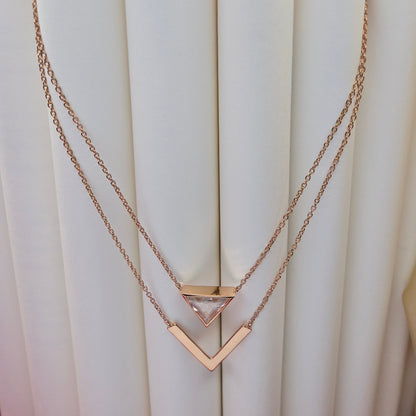 Layered rose-gold plated necklace featuring a clear triangular-cut stone pendant on the upper chain and a sleek V-shaped bar pendant on the lower chain, perfect for contemporary everyday styling.