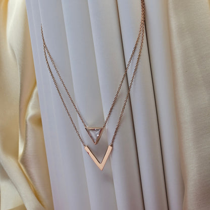 Layered rose-gold plated necklace featuring a clear triangular-cut stone pendant on the upper chain and a sleek V-shaped bar pendant on the lower chain, perfect for contemporary everyday styling.