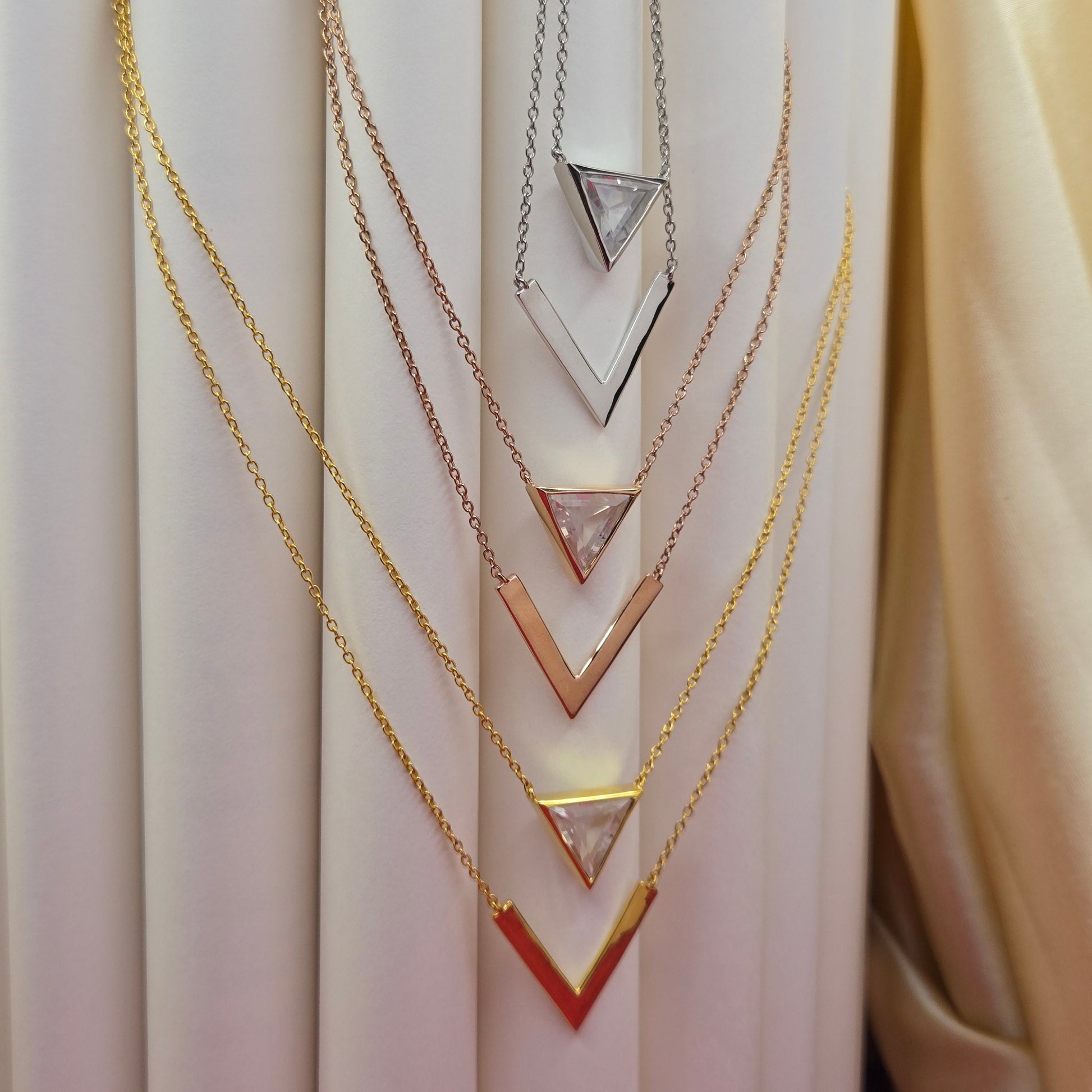 Layered gold, rose-gold, rhodium plated necklace featuring a clear triangular-cut stone pendant on the upper chain and a sleek V-shaped bar pendant on the lower chain, perfect for contemporary everyday styling.