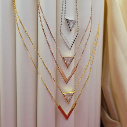 Layered gold, rose-gold, rhodium plated necklace featuring a clear triangular-cut stone pendant on the upper chain and a sleek V-shaped bar pendant on the lower chain, perfect for contemporary everyday styling.