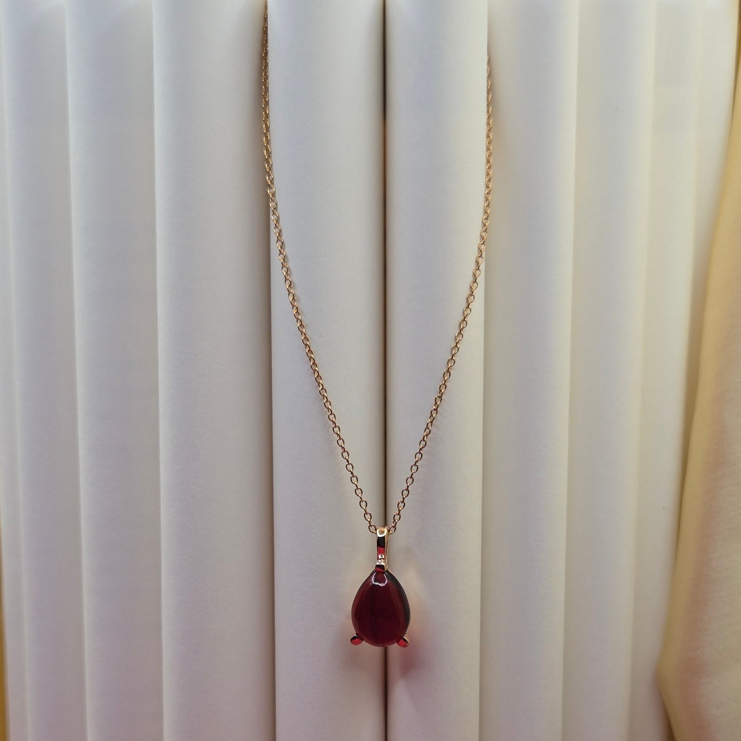 Gold-plated chain necklace featuring a smooth teardrop-shaped deep maroon gemstone pendant, styled against a soft neutral backdrop for an elegant and minimal look.