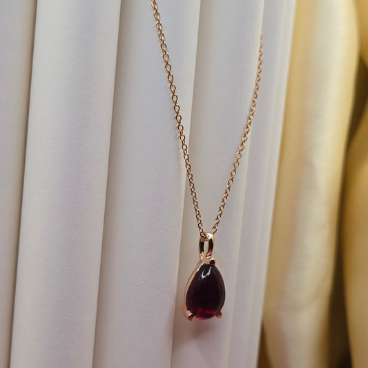 Rose gold plated chain necklace featuring a smooth teardrop-shaped deep maroon gemstone pendant, styled against a soft neutral backdrop for an elegant and minimal look.