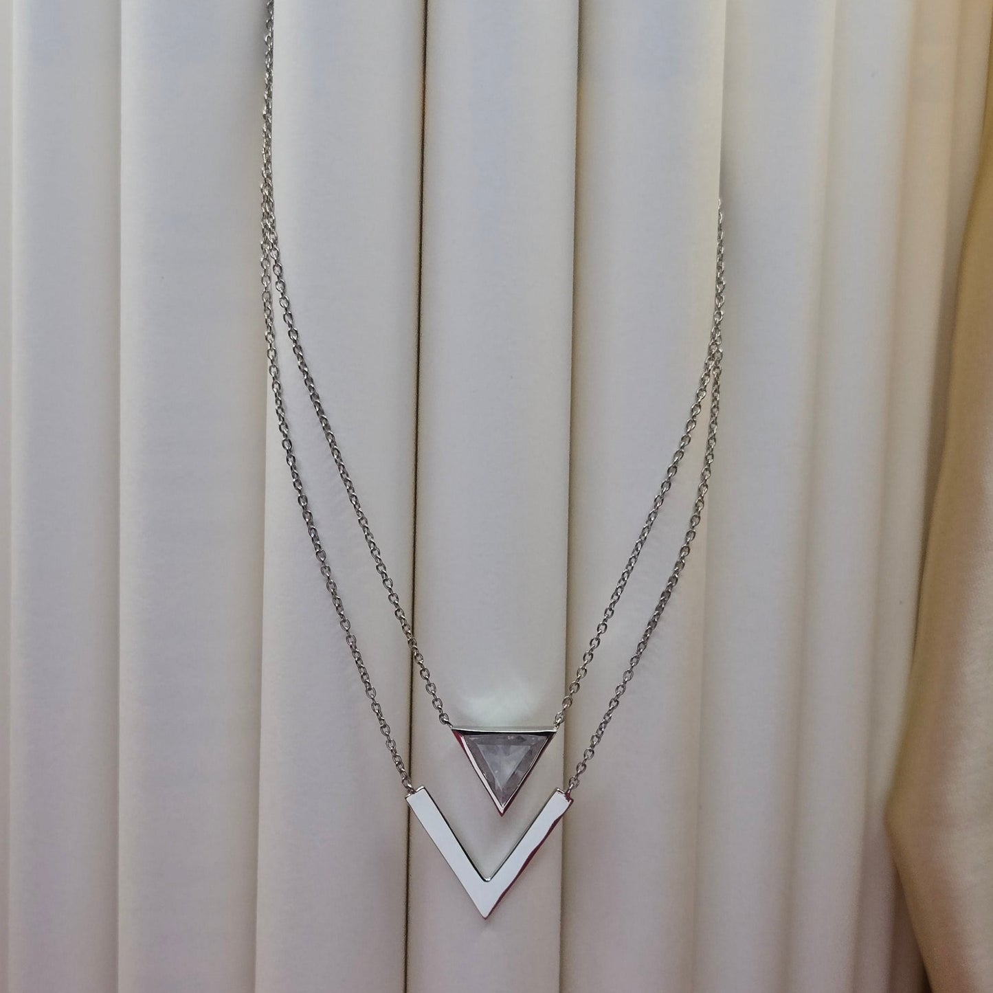 Layered rhodium plated necklace featuring a clear triangular-cut stone pendant on the upper chain and a sleek V-shaped bar pendant on the lower chain, perfect for contemporary everyday styling.