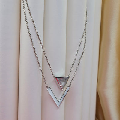 Layered rhodium plated necklace featuring a clear triangular-cut stone pendant on the upper chain and a sleek V-shaped bar pendant on the lower chain, perfect for contemporary everyday styling.