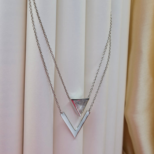 Layered rhodium plated necklace featuring a clear triangular-cut stone pendant on the upper chain and a sleek V-shaped bar pendant on the lower chain, perfect for contemporary everyday styling.