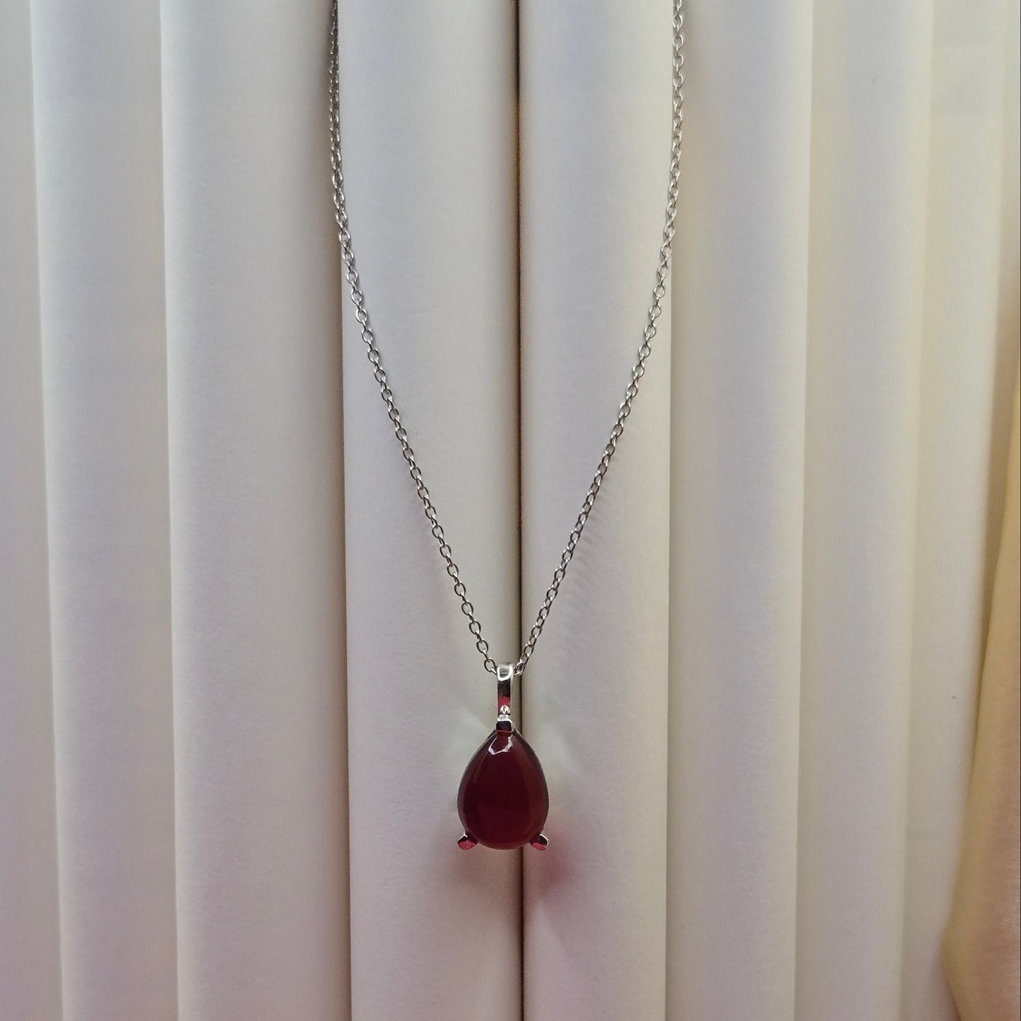 Rhodium plated chain necklace featuring a smooth teardrop-shaped deep maroon gemstone pendant, styled against a soft neutral backdrop for an elegant and minimal look.