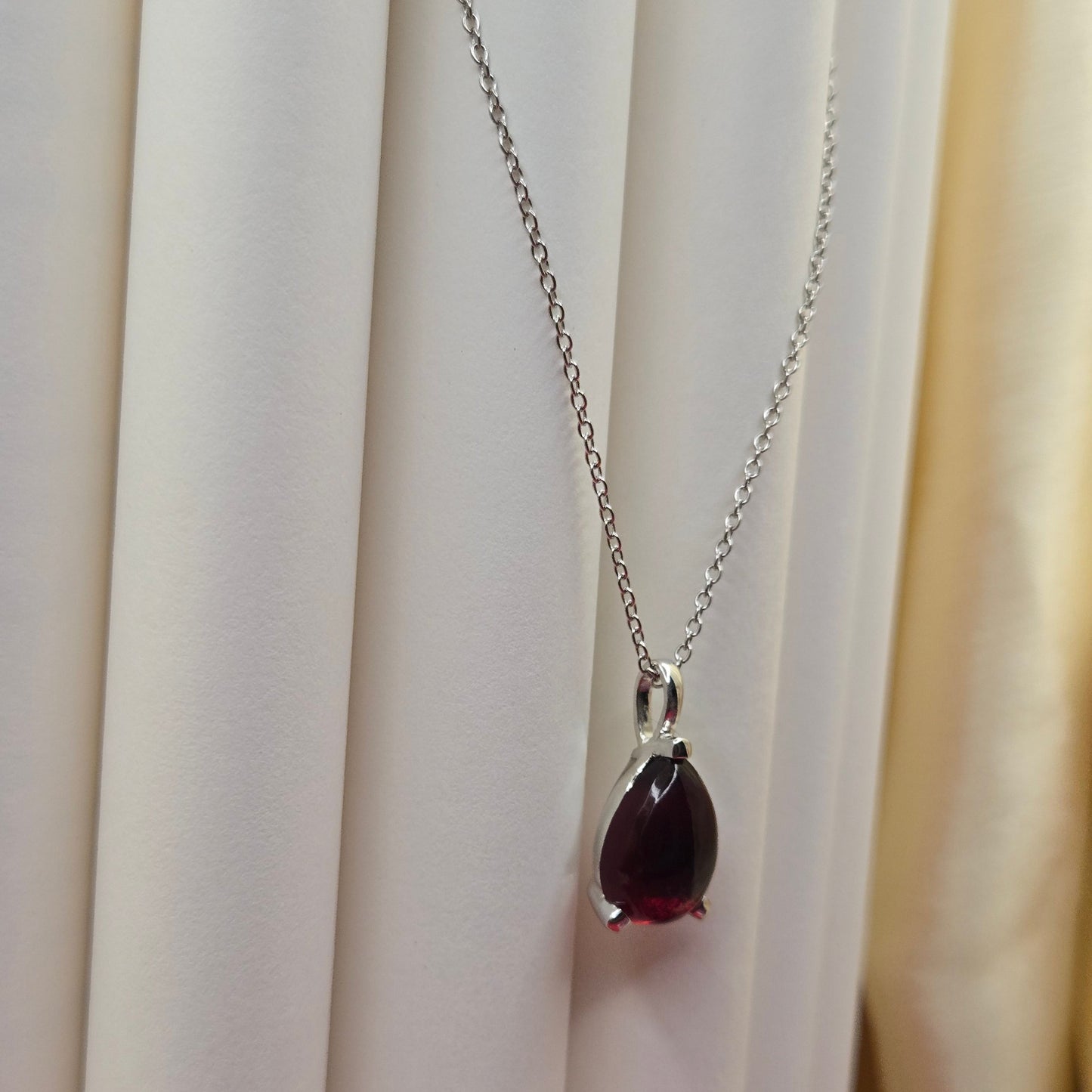 Rhodium plated chain necklace featuring a smooth teardrop-shaped deep maroon gemstone pendant, styled against a soft neutral backdrop for an elegant and minimal look.