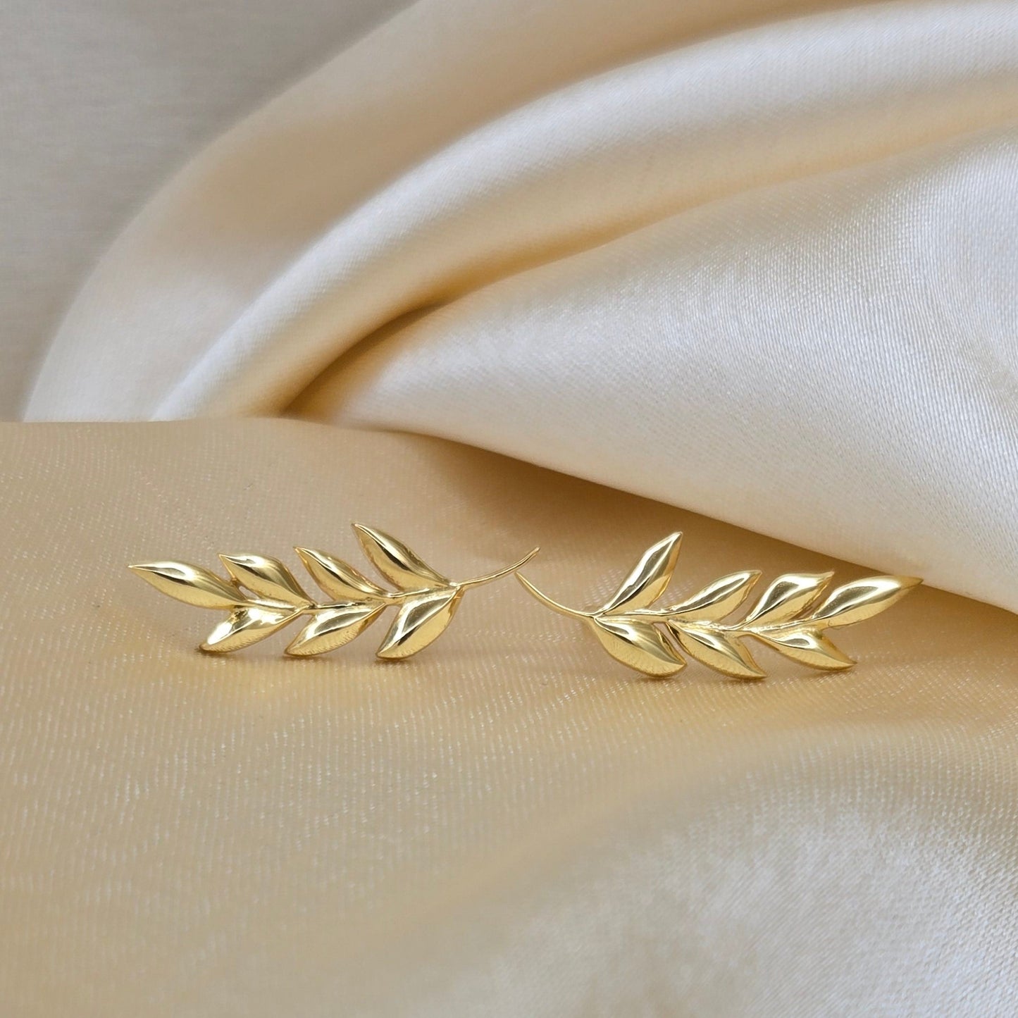 Gold leaf-shaped earrings on a soft beige fabric background