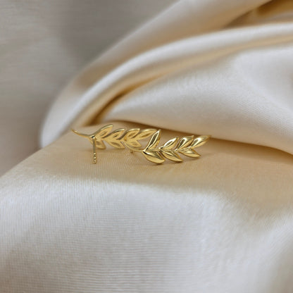 Gold leaf-shaped earring on a beige fabric background