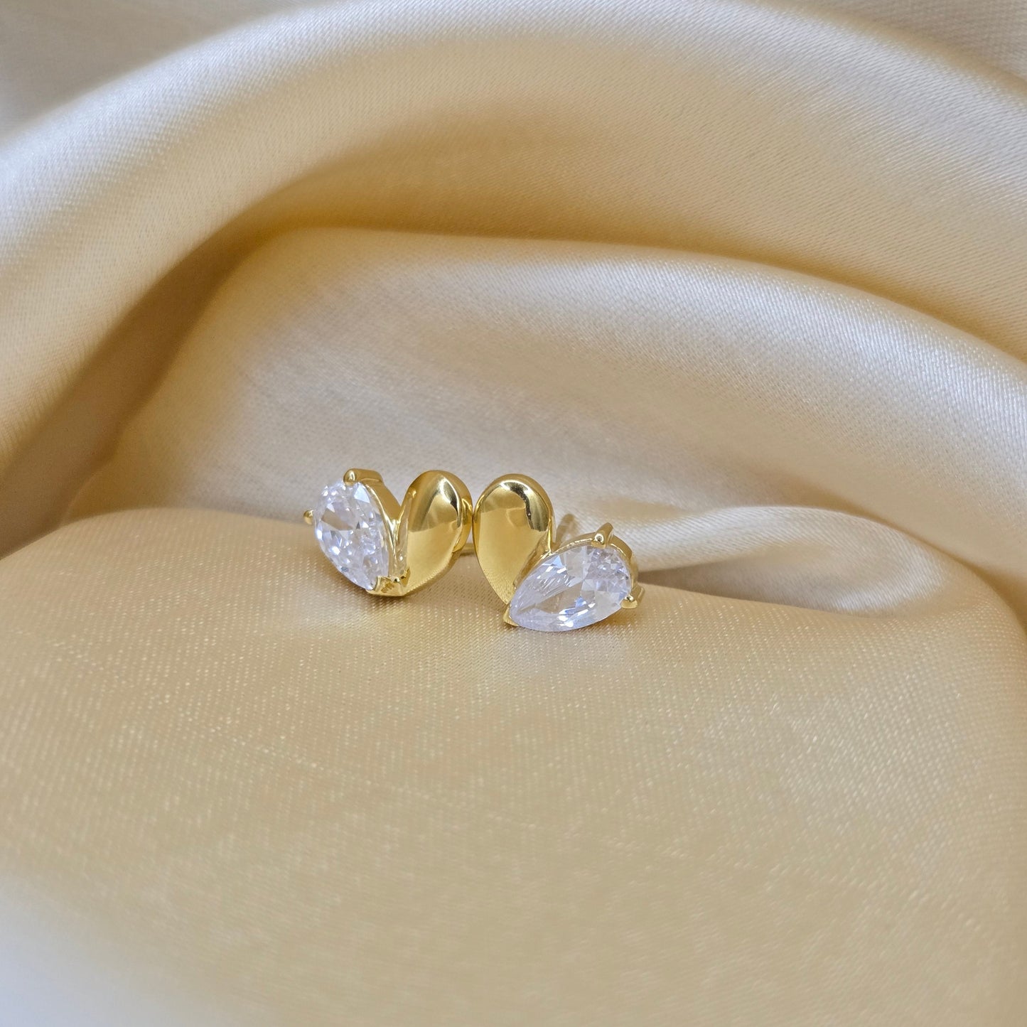 Gold earring with clear gemstones on a beige fabric background