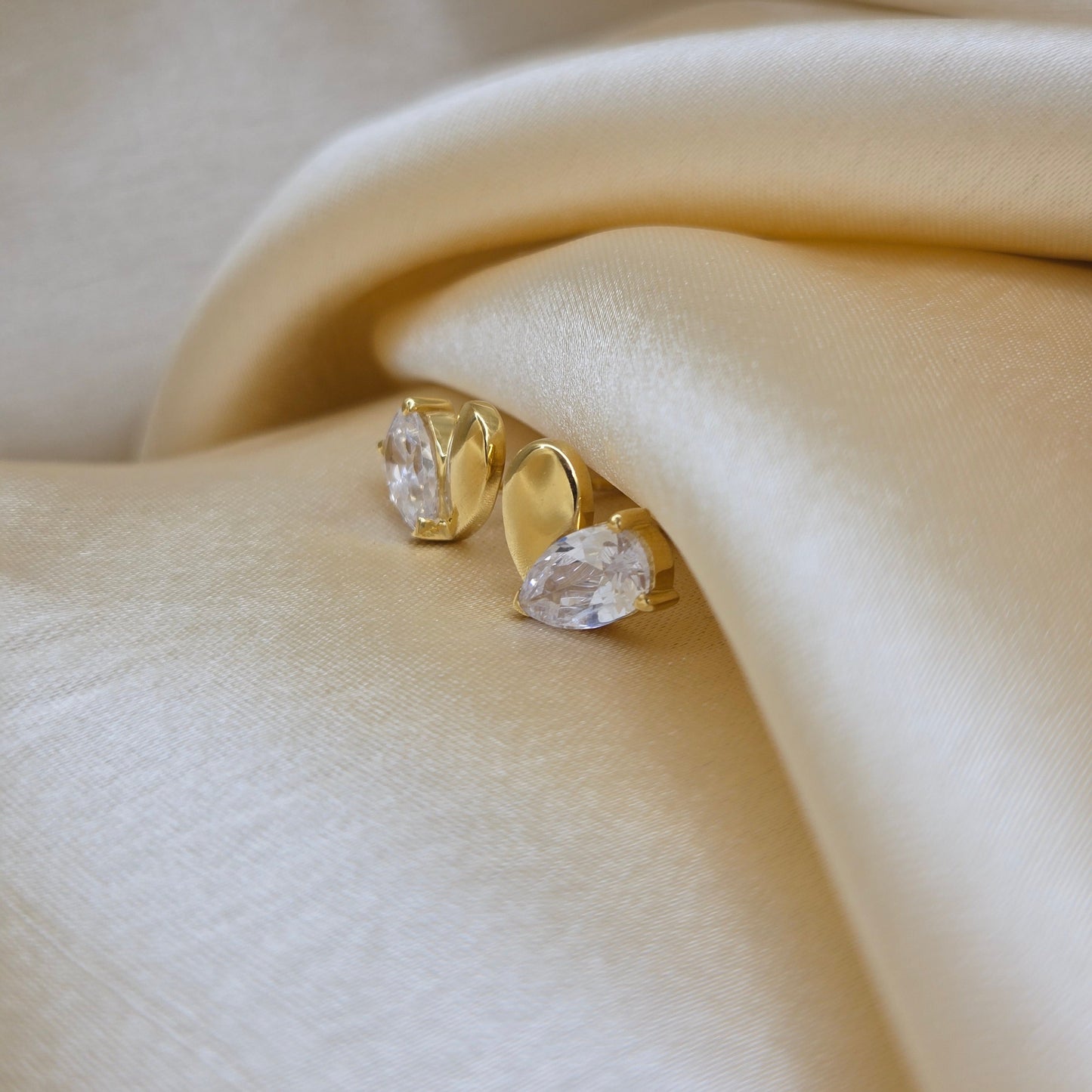 Gold earrings with clear gemstones on a soft beige fabric background