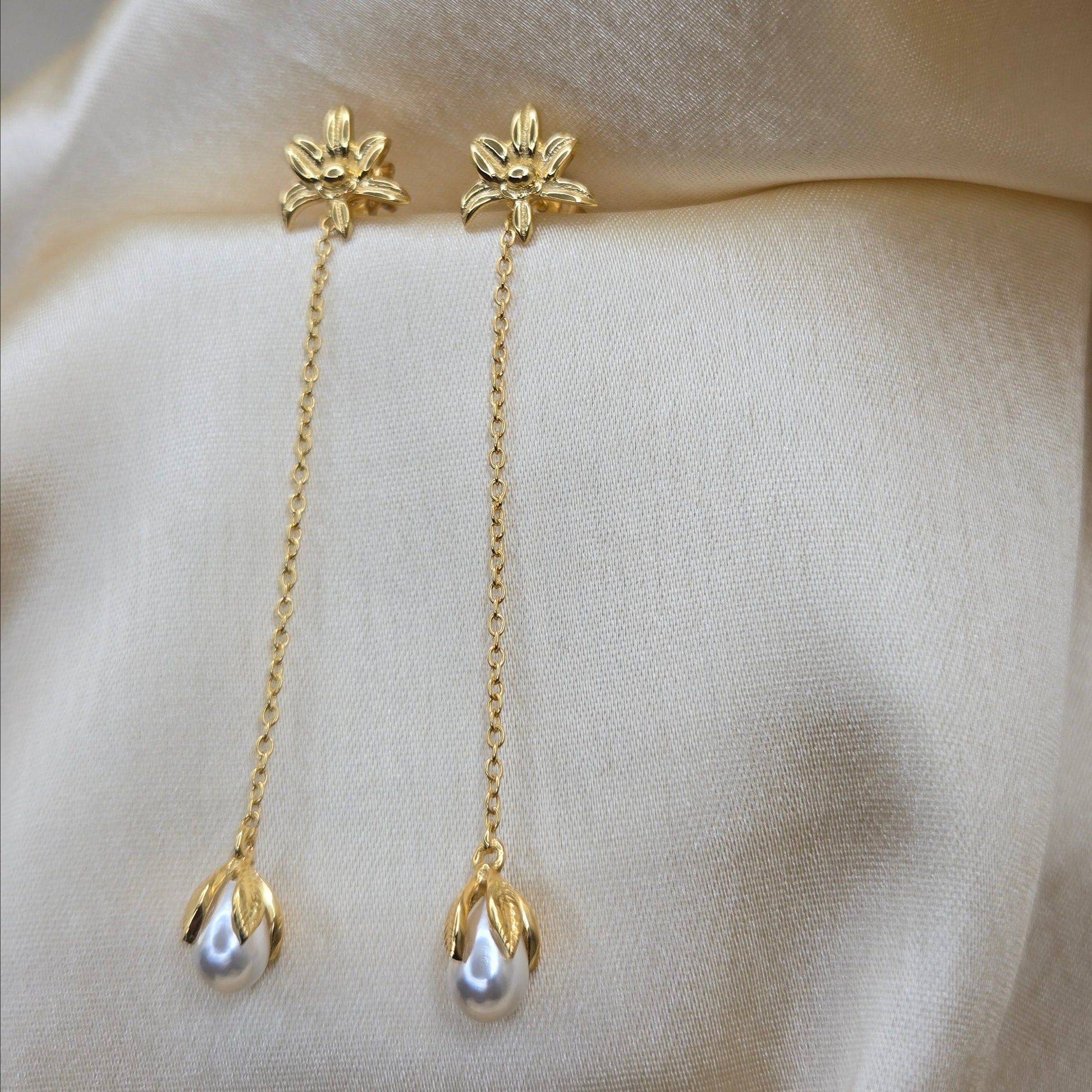 Lightweight gold chain dangle earrings with pearl buds and intricate flower detailing, photographed on luxurious ivory satin for a refined and romantic aesthetic.