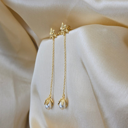 Lightweight gold chain dangle earrings with pearl buds and intricate flower detailing, photographed on luxurious ivory satin for a refined and romantic aesthetic.
