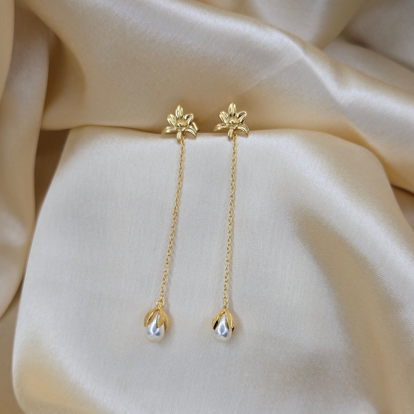 Lightweight gold chain dangle earrings with pearl buds and intricate flower detailing, photographed on luxurious ivory satin for a refined and romantic aesthetic.