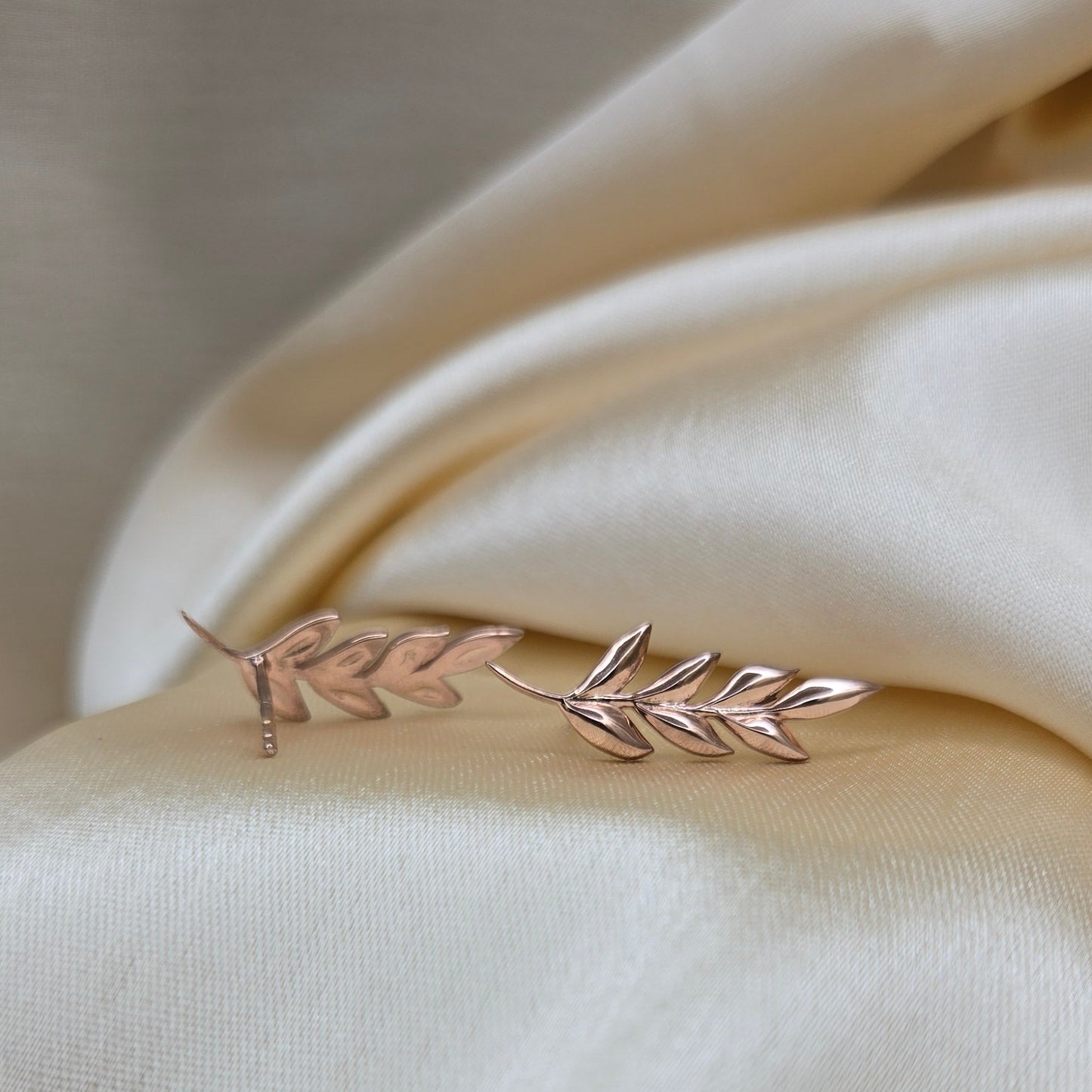 Delicate gold leaf earring on a soft beige fabric background