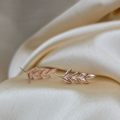 Delicate gold leaf earring on a soft beige fabric background