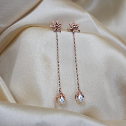 Lightweight rose-gold chain dangle earrings with pearl buds and intricate flower detailing, photographed on luxurious ivory satin for a refined and romantic aesthetic.