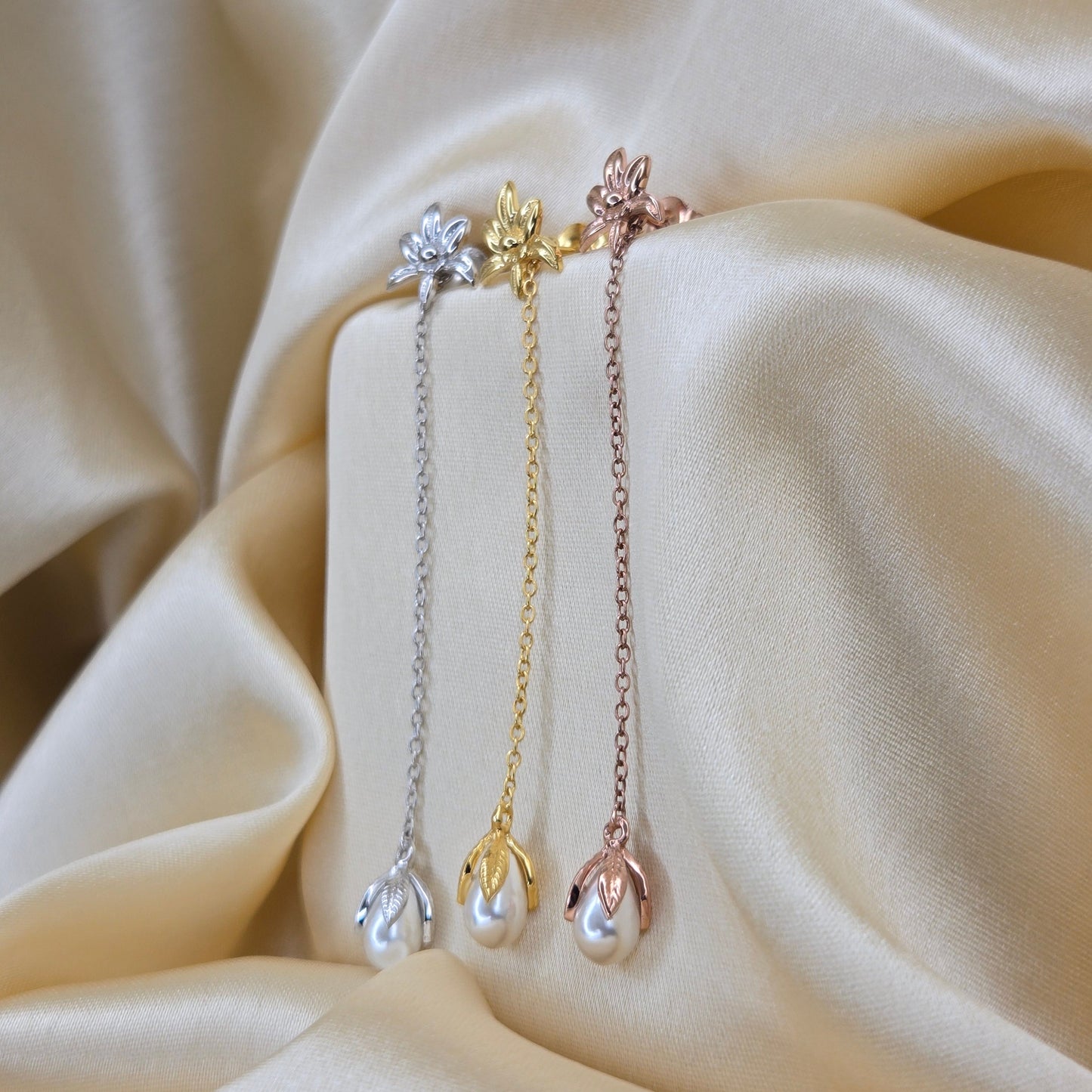 Lightweight gold, rose-gold & rhodium chain dangle earrings with pearl buds and intricate flower detailing, photographed on luxurious ivory satin for a refined and romantic aesthetic.