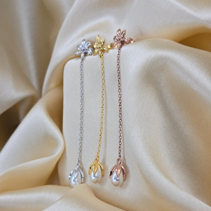 Lightweight gold, rose-gold & rhodium chain dangle earrings with pearl buds and intricate flower detailing, photographed on luxurious ivory satin for a refined and romantic aesthetic.