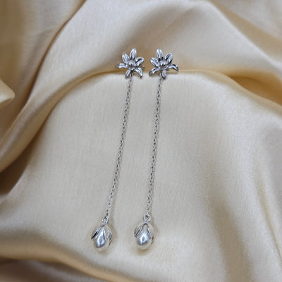 Lightweight rhodium chain dangle earrings with pearl buds and intricate flower detailing, photographed on luxurious ivory satin for a refined and romantic aesthetic.