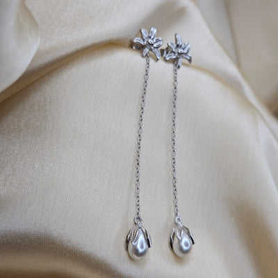 Lightweight rhodium chain dangle earrings with pearl buds and intricate flower detailing, photographed on luxurious ivory satin for a refined and romantic aesthetic.