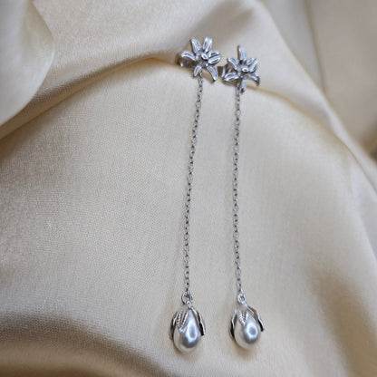 Lightweight rhodium chain dangle earrings with pearl buds and intricate flower detailing, photographed on luxurious ivory satin for a refined and romantic aesthetic.