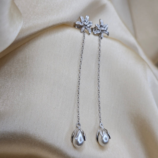 Lightweight rhodium chain dangle earrings with pearl buds and intricate flower detailing, photographed on luxurious ivory satin for a refined and romantic aesthetic.