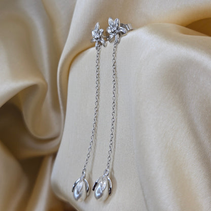 Lightweight rhodium chain dangle earrings with pearl buds and intricate flower detailing, photographed on luxurious ivory satin for a refined and romantic aesthetic.